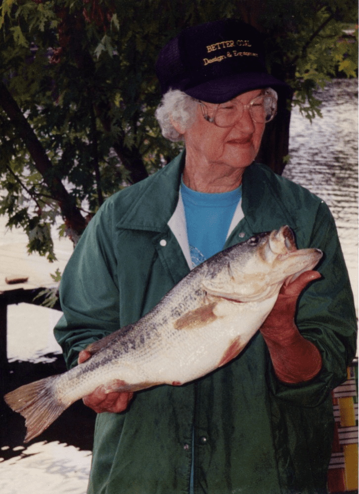 The grandson is fishing with his grandmother on the river bank.  Fishermen with a fishing rod in the summer. A little boy with a grandmother  puts a bait on a fishing