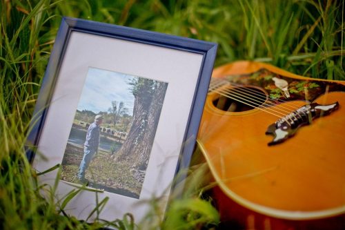 picture of man laying against guitar in the grass