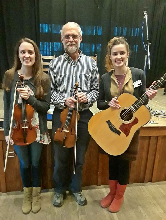 a girl and a man holding fiddles standing with a girl holding a guitar