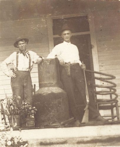 old photo of two men standing by moonshine still