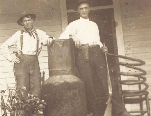 old photo of two men standing by moonshine still