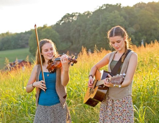 The Pressley Girls standing in a field of grass smiling with instruments