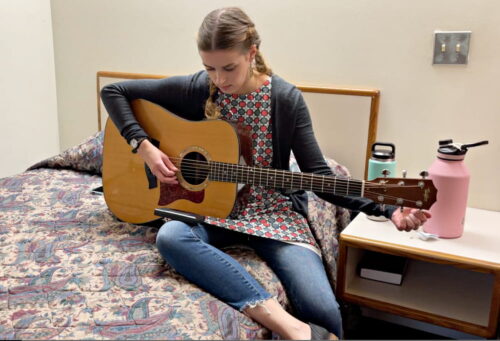 Corie tuning guitar on bed