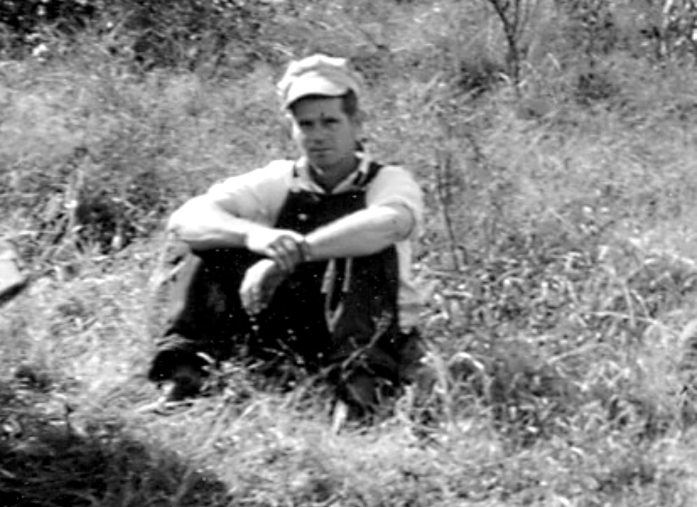 Man sitting in field with hat and overalls